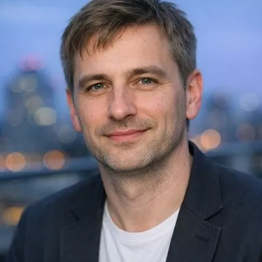 Dark-blonde man in his early forties, cool grey-green gaze, dark blazer